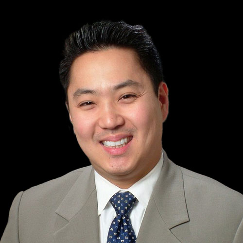 Professional headshot of ophthalmologist Dr. Brian M. Chang, in a light suit and blue patterned tie, smiling confidently against a black background.