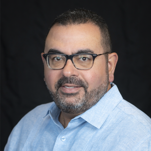 Professional headshot of ophthalmologist Dr. Carlos Diaz, wearing glasses and a light blue shirt, smiling against a black background.