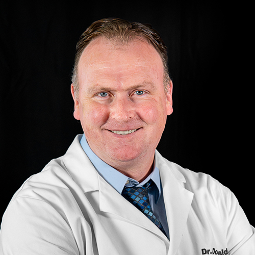 Professional headshot of ophthalmologist Dr. Joseph M. Donaldson, wearing a white coat and patterned tie, smiling in front of a dark background.