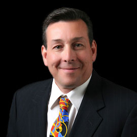 Portrait of Dr. Leland Sherlock, optometrist at Southwestern Eye Center, wearing a dark suit and striped tie, smiling with a professional demeanor.