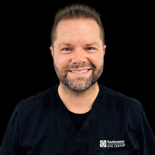 Professional headshot of optometrist Dr. Michael Rollins, wearing black scrubs, smiling against a black background.