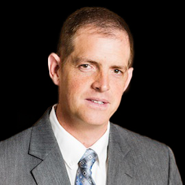 Professional headshot of optometrist Dr. James Hooper, in a light gray suit and patterned tie, posed against a black background.