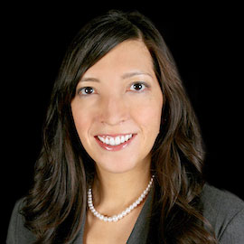 Professional headshot of optometrist Dr. Jennifer Murray, wearing a dark blazer and pearl necklace, smiling in front of a black background.