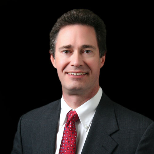 Professional headshot of ophthalmologist Dr. Daryl Pfister, wearing a dark suit and red patterned tie, posed against a painted studio backdrop.