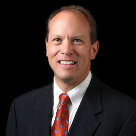 Professional headshot of optometrist Dr. Arlynn B. Roper, wearing a red tie and suit, smiling against a painted neutral background.