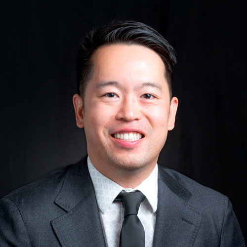 Portrait of Dr. Bailey Yee, optometrist at Southwestern Eye Center, smiling warmly, wearing a dark suit and tie with a neutral background.