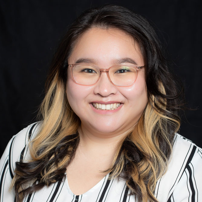 Laura-Liz Encarnacion, O.D., is professionally dressed in a white blouse with black stripes. She is featured on a black neutral backdrop.