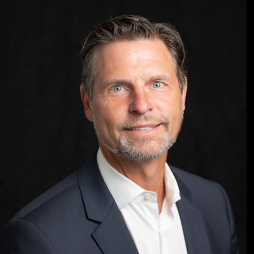 Professional headshot of optometrist Dr. David Fairley, in a dark blazer and open-collared shirt, smiling in front of a dark background.