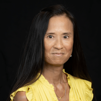 Professional headshot of ophthalmologist Dr. Carol Lee-Faust, wearing a yellow sleeveless top and smiling softly against a black background.