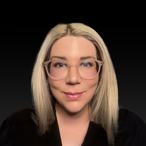 Professional headshot of ophthalmologist Dr. Lucy Mudie, with straight blonde hair and glasses, wearing a black scrubs against a black backdrop.