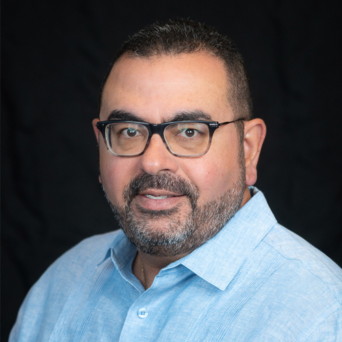 Professional headshot of ophthalmologist Dr. Carlos Diaz, wearing glasses and a light blue shirt, smiling against a black background.