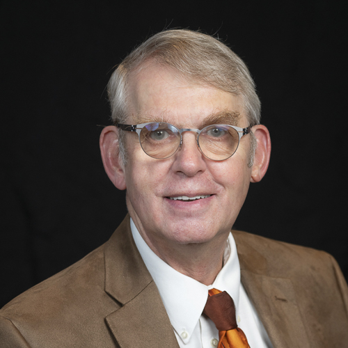 Professional headshot of ophthalmologist Dr. John Malin Lewis, wearing glasses and a brown jacket with an orange tie, posed against a black backdrop.
