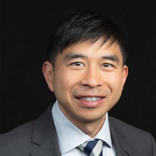 Professional headshot of ophthalmologist Dr. Wen-Shin Lee, in a gray suit and patterned tie, smiling confidently against a dark background.