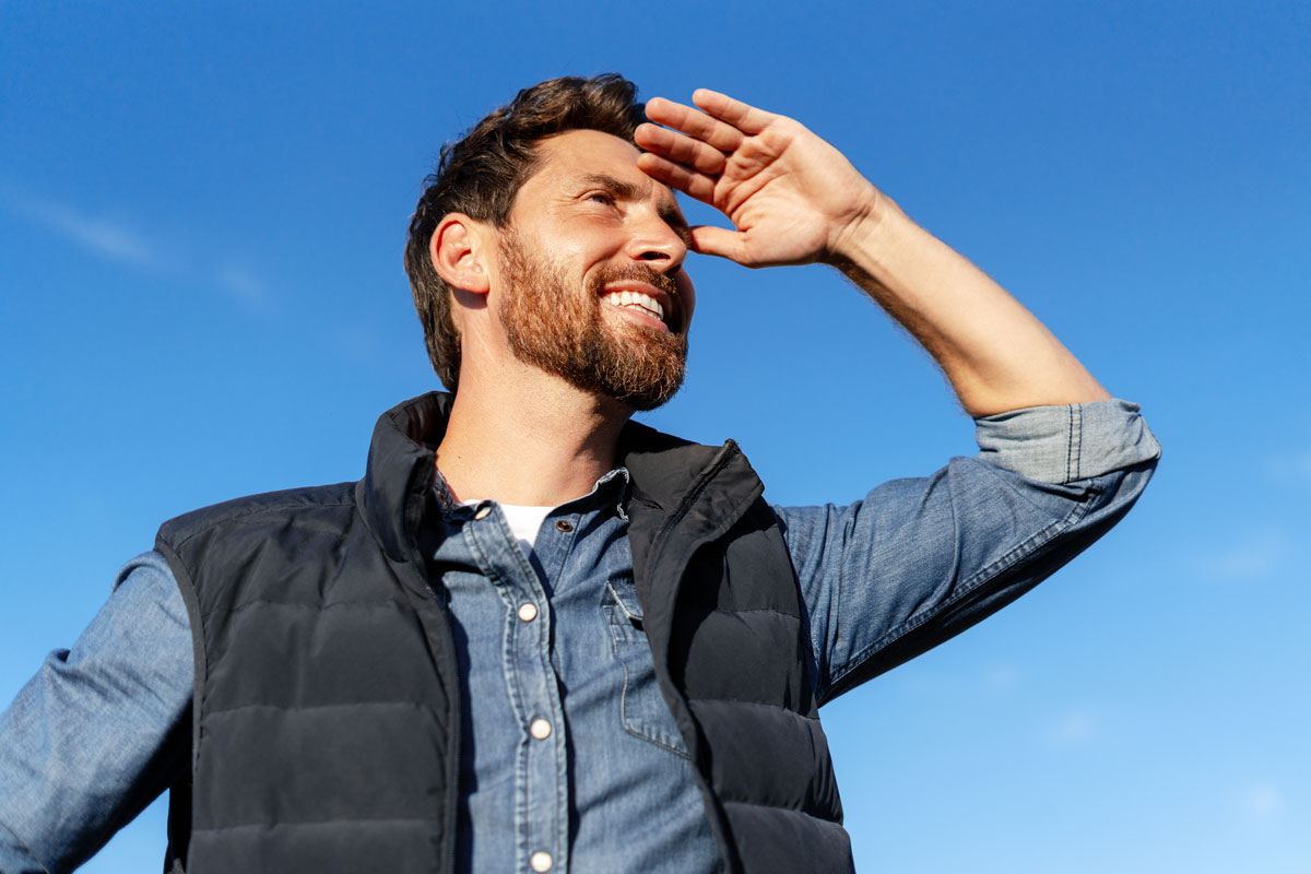 Man smiling outdoors while shielding eyes from sunlight after LASIK surgery