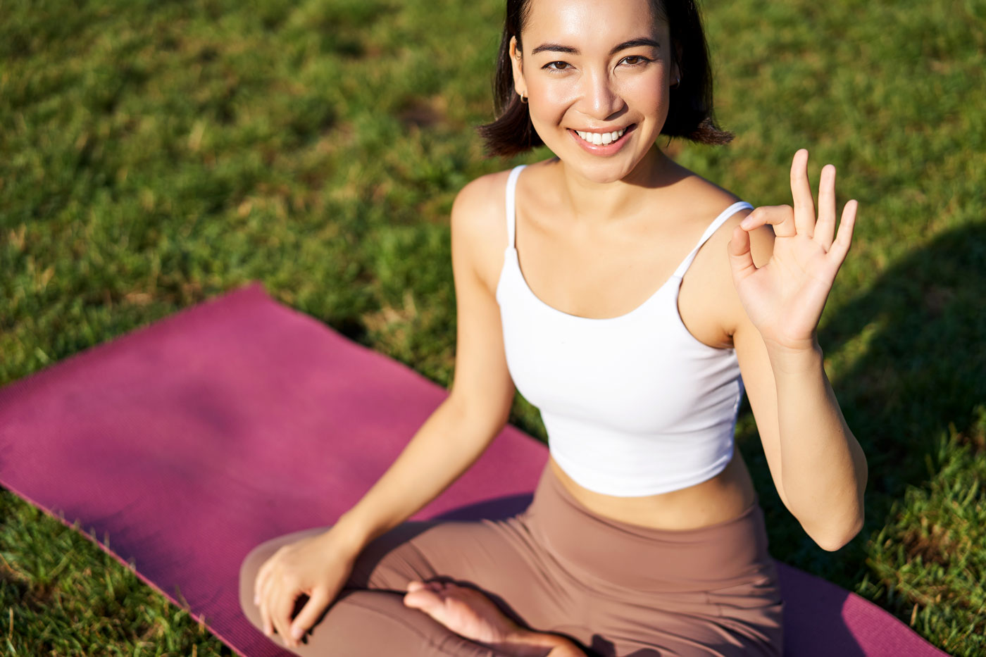 common LASIK fears woman sitting outdoors on a yoga mat making an “OK” hand gesture, symbolizing confidence and calm about LASIK surgery.
