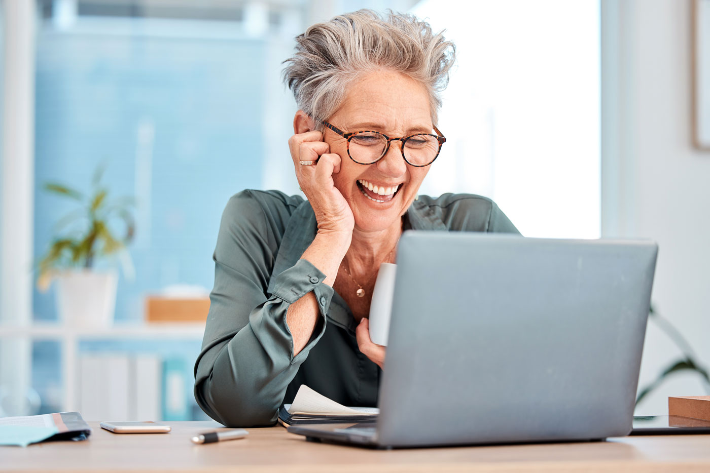 Smiling older adult at laptop learning the differences between glaucoma and cataracts and how much cataract surgery costs.