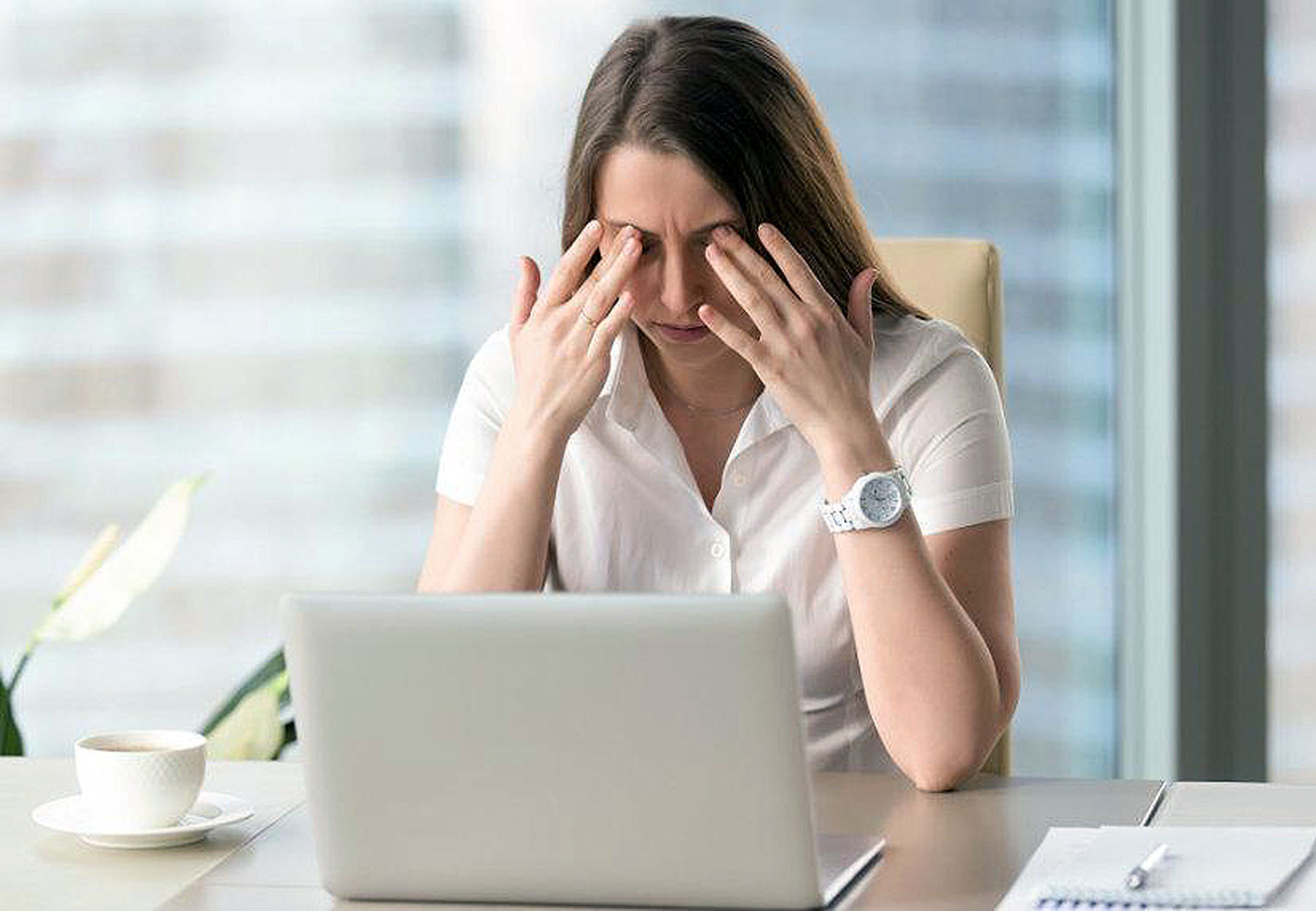 Young woman suffereing from eyelid twitching at work, rubbing her eyes, learn more at Southwestern Eye Center.