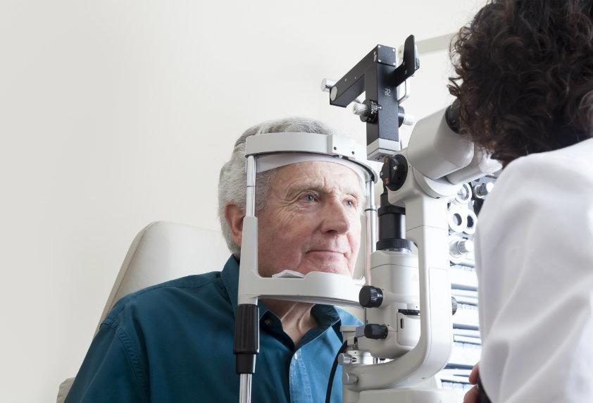 Older patient receiving a slit lamp eye exam from an ophthalmologist to evaluate corneal damage and determine need for corneal transplant.