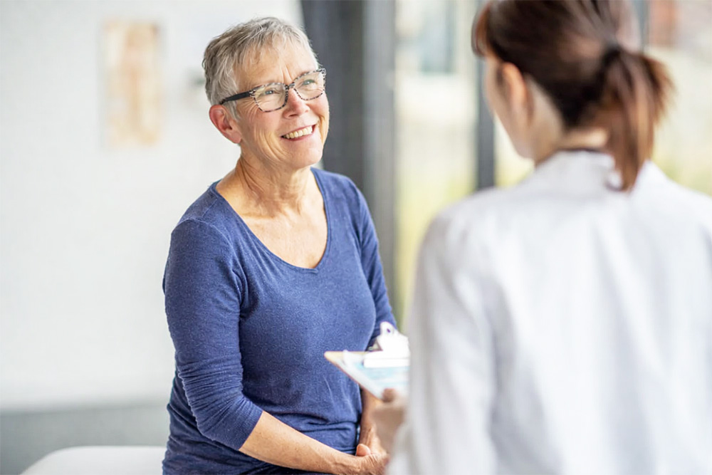 Smiling older woman speaking with a healthcare provider during an eye exam consultation, representing early detection and discussion of retina damage and vision health.