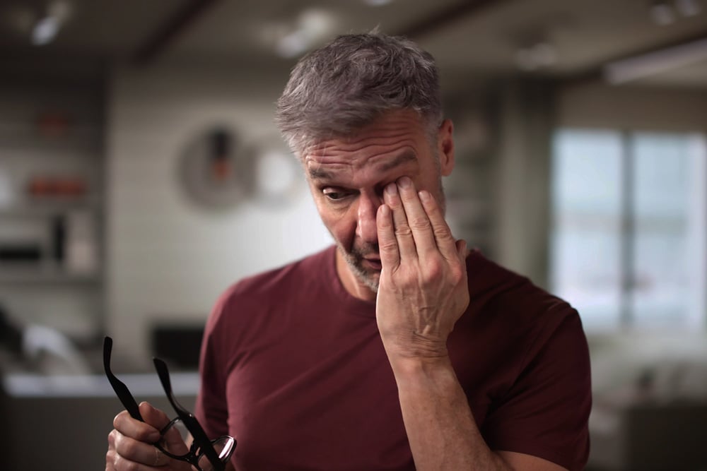 Man rubbing his irritated eye, illustrating common causes of dry eye such as screen strain, fatigue, and reduced tear production.