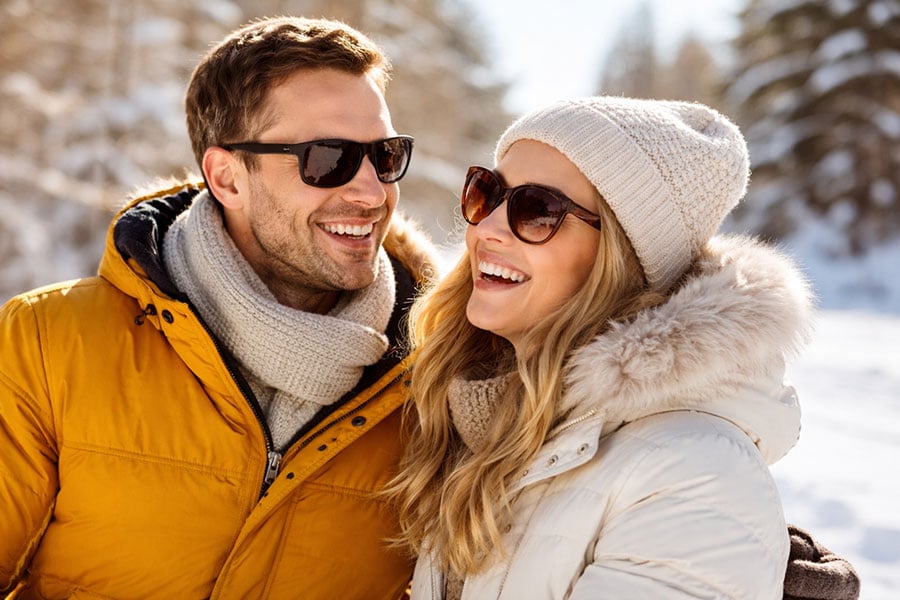 Couple wearing sunglasses in a bright snowy winter setting, highlighting eye protection from sun glare and UV exposure.