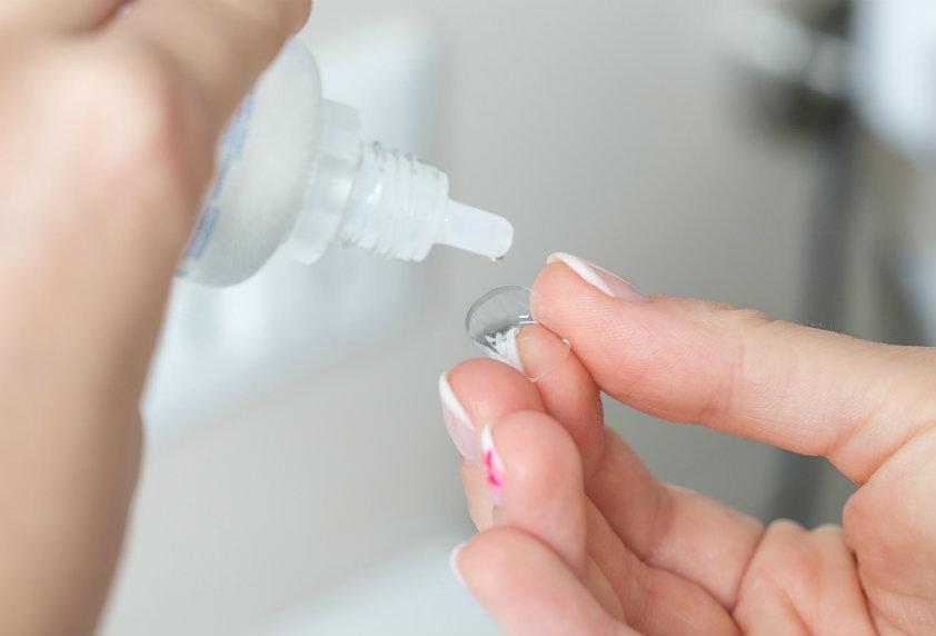 Contact lens being cleaned with solution to reduce the long-term effects of contact lenses on eye health and prevent infection.