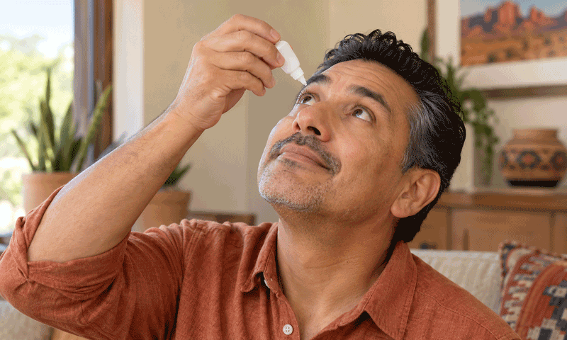 Man comfortably applying eye drops to one eye at home