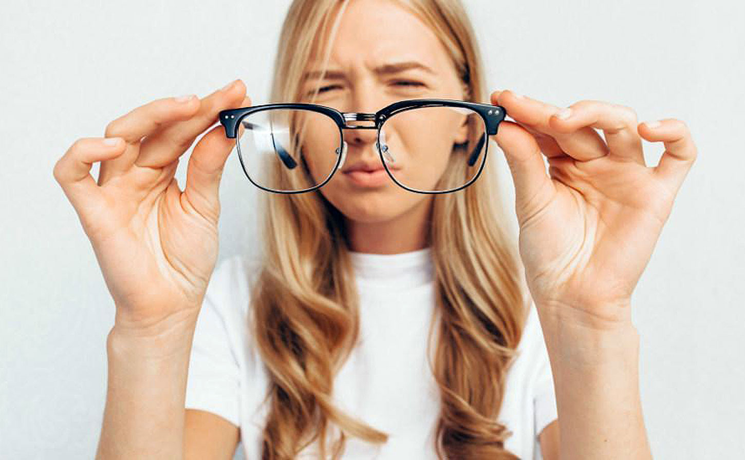 What are those floaters in your eyes? Young blond woman holding glasses out and squinting - Southwestern Eye Center.