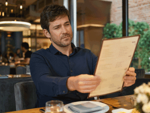 Man suffering from presbyopia, having trouble reading the food menu at a restaurant. Southwestern Eye Center.