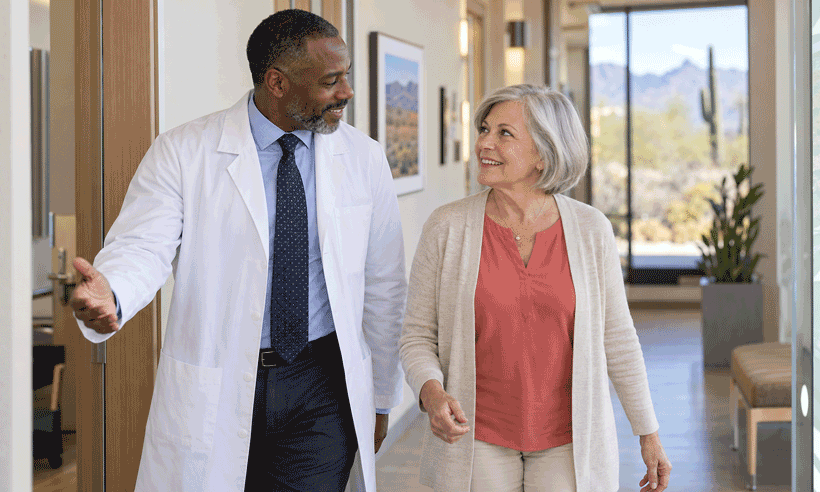 Eye doctor walks through a bright clinic with an older woman as they smile and talk.